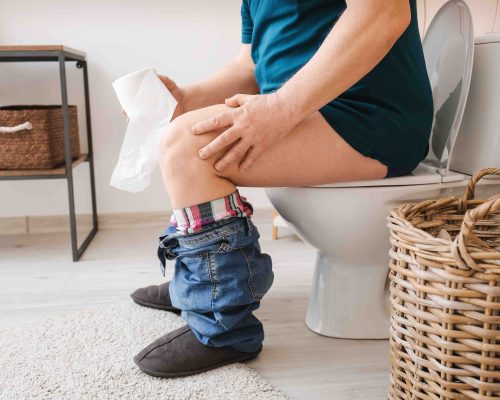 Elderly man with hemorrhoids sitting on toilet bowl in restroom