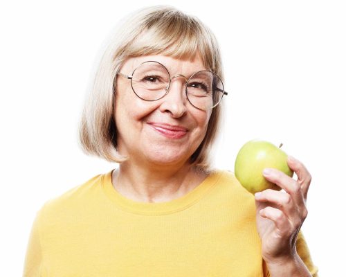 Portrait of a beautiful elderly woman wearing glasses holding an apple, smiling, isolated on white background. Happy Woman Holding Granny Smith Apple.